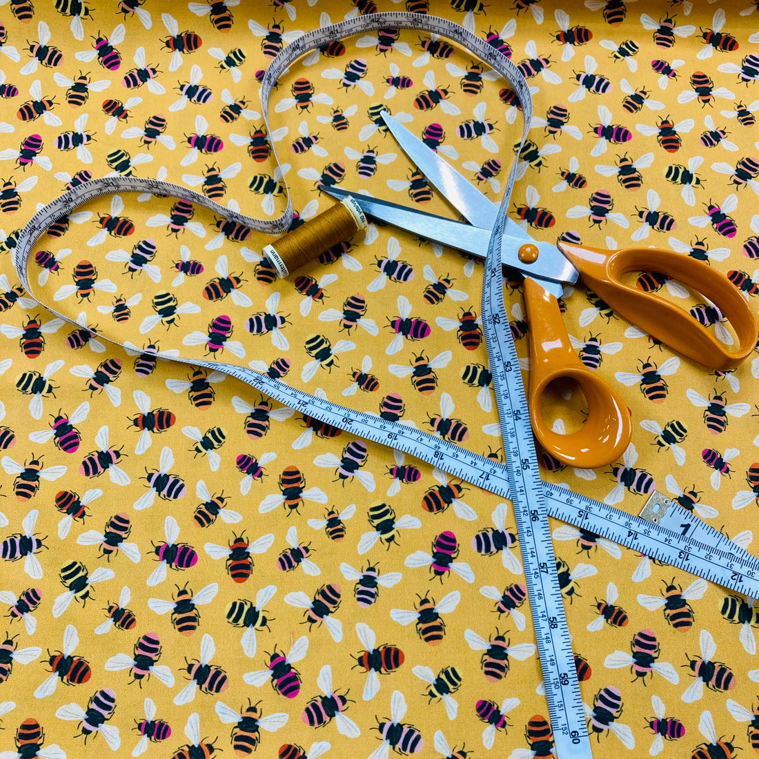 Bee themed fabric with scissors, a tape measure and thread.